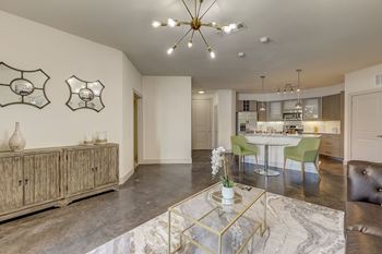 A modern living room with a glass coffee table and a dining table in the background.